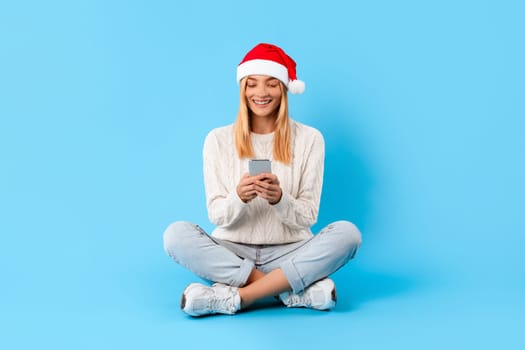 Happy woman with smartphone wearing Santa hat