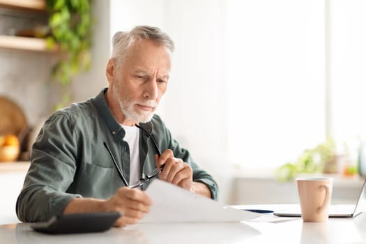 Elderly man reviewing documents while sitting at kitchen desk