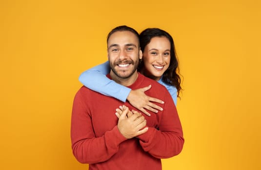Portrait of joyful millennial woman hugging her boyfriend from behind
