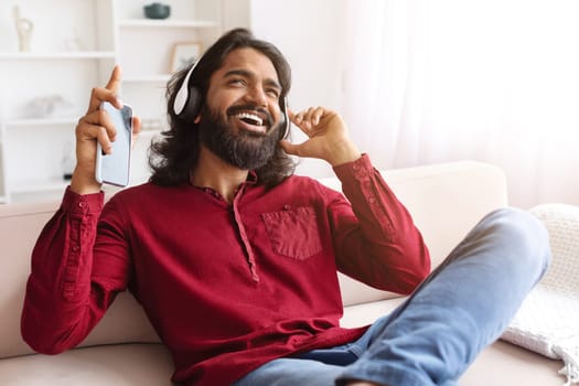 Happy guy resting on sofa at home, listening to music