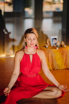 Meditation and concentration. a woman in a red dress, sitting on the floor with her eyes closed, is practicing medicine indoors. Peace and relaxation