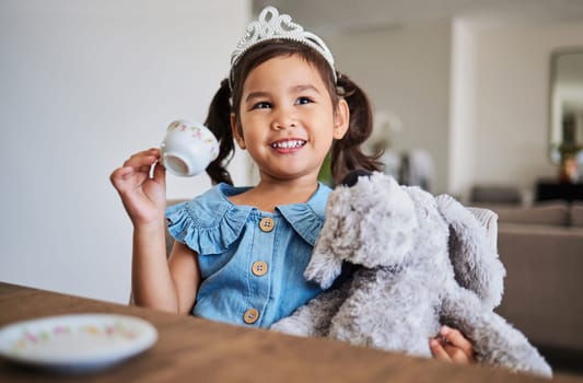 Children, imagination and tea party with a girl playing pretend at a table in her home alone. Kids, happy and game with a young female child drinking from a cup with a teddy bear in her house