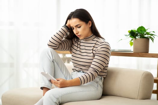 Sad unhappy millennial arab woman typing by phone at sofa, chatting, suffer from bad news
