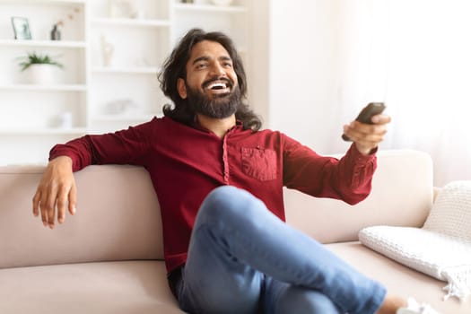 Emotional indian man watching TV at home, laughing