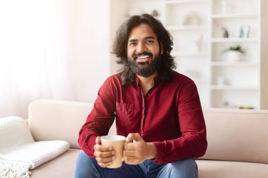 Cool positive indian man enjoying morning coffee at home