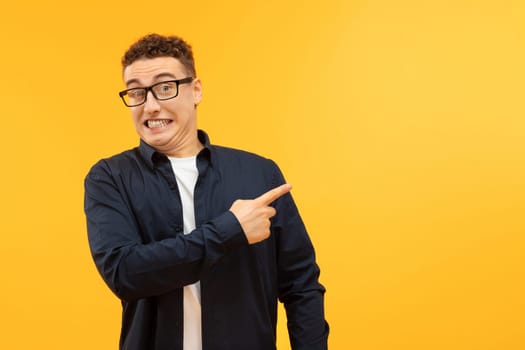 Funny blonde guy pointing at copy space, yellow background