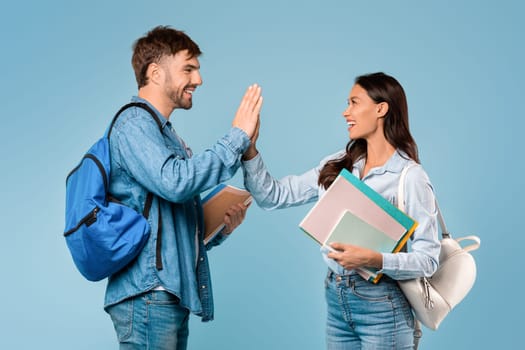 Happy male and female students high five with books, blue background