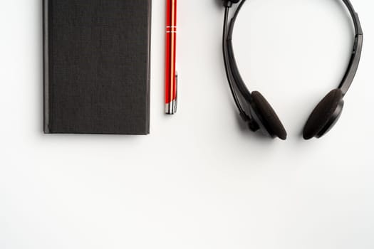 Black notebook, headset and pen on white background