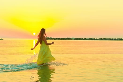 Beautiful woman walking in water wearing a yellow colorful dress.