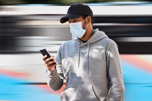 Man in city with mask, phone and waiting at bus stop to travel, checking service schedule or social media. Public transport safety in covid, urban commute and person in street with smartphone app.