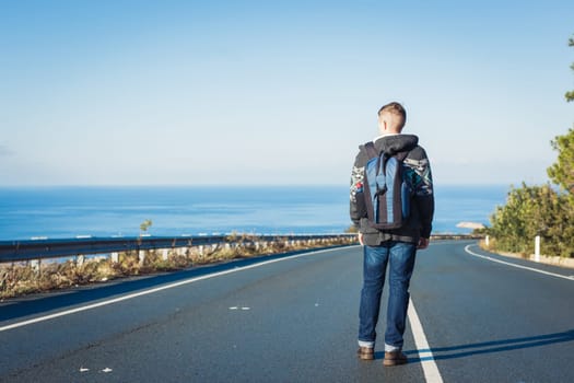 Young man with a backpack walks alone on a road