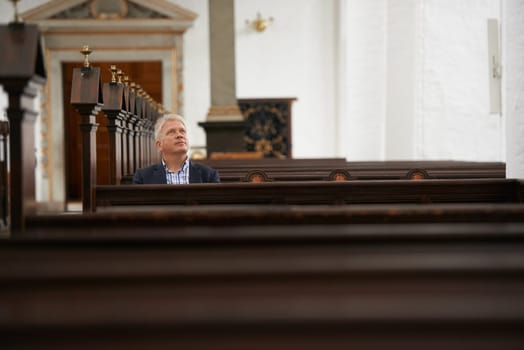 Senior man, sitting and church for religion, faith or pray at cathedral or holy grounds in Jesus Christ. Mature or religious male person looking up in sanctuary for salvation, forgiveness or worship