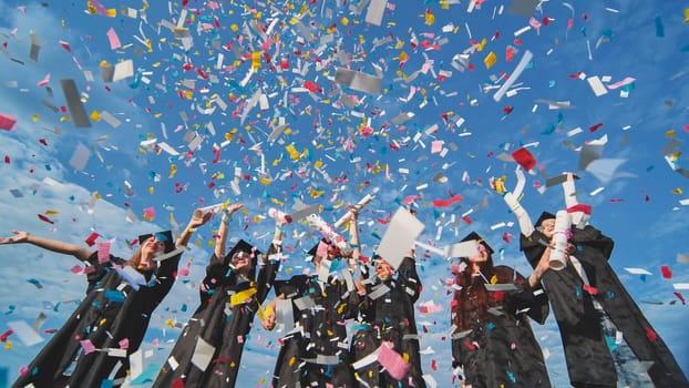 Graduates throw colorful confetti against a blue sky.