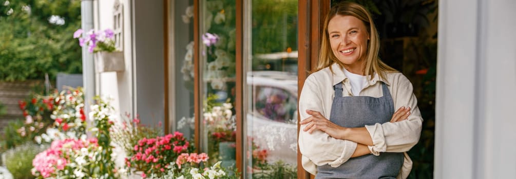 Smiling woman florist small business owner standing with crossed arms near own floral store