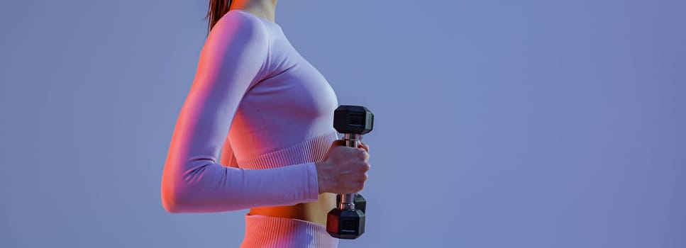 Side view of fitness woman doing exercises with dumbbells on studio background