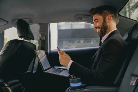 Smiling entrepreneur working on laptop and use mobile phone while going to airport by car