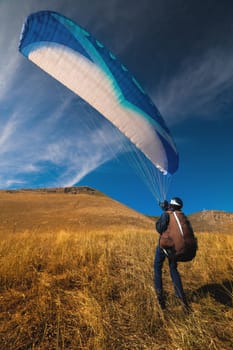 A paraglider is preparing to take off from a mountain on a sunny day. paraglider taking off from yellow grass, against the background of blue sky and mountains.