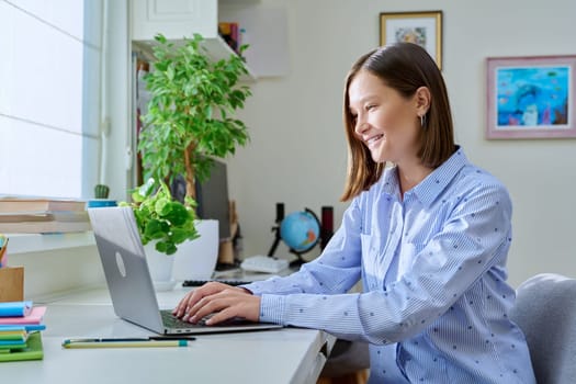 Young smiling woman typing on laptop computer at home
