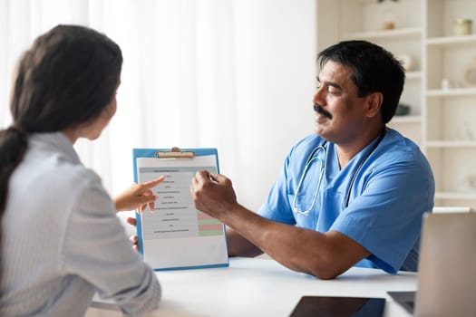 Mature Indian Doctor Consulting Patient Before Medical Check Up In Clinic