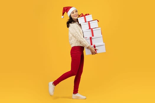 woman carrying tower of festive Xmas boxes on yellow backdrop