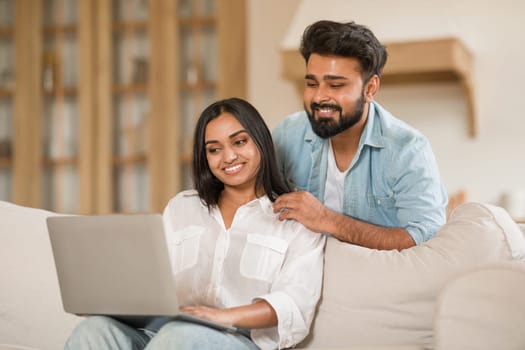 Indian man and woman with laptop, comfortable on sofa.