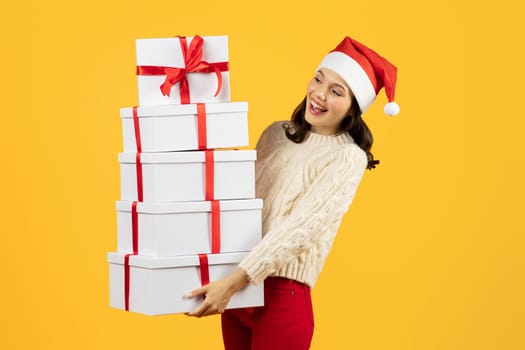 Happy woman with stack of wrapped Christmas presents, yellow background