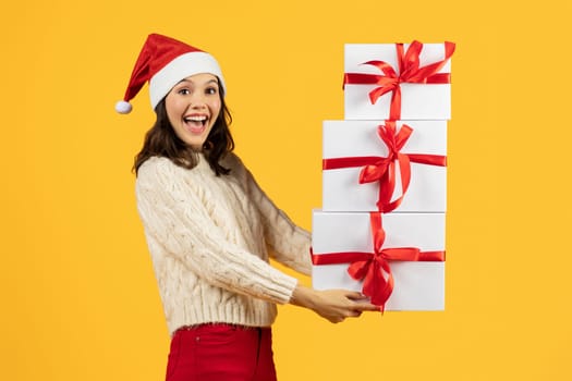 woman posing with stack of Christmas gifts on yellow background