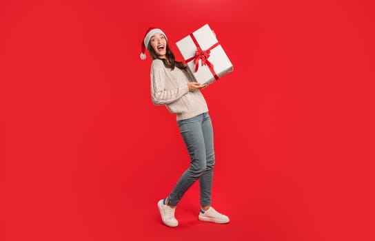 woman in Santa hat holding festive gift on red background