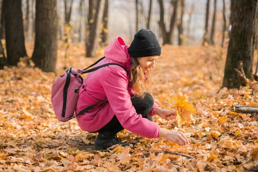 Young woman in a hat collects autumn leaves. Fall season concept. Generation Z and gen z youth