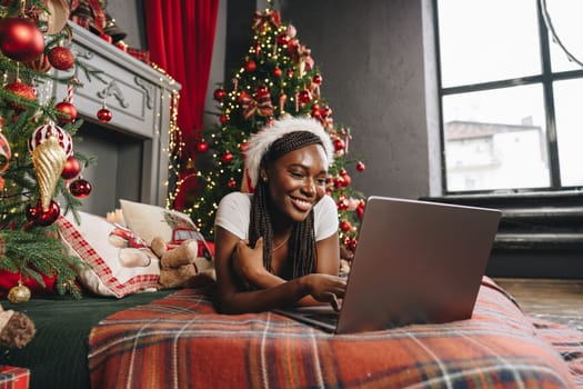 Young African woman on bed using laptop on Christmas eve