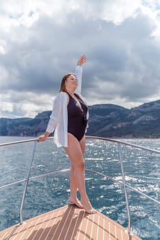 Woman on a yacht. Happy model in a swimsuit posing on a yacht against a blue sky with clouds and mountains