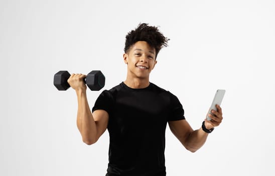 Athletic hispanic man grips dumbbell and smartphone over white background