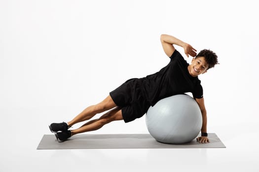 man performs side plank exercise on balance ball, white background
