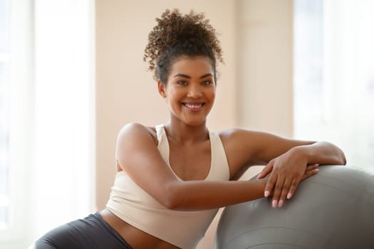 Fit young lady takes rest on exercise ball indoors