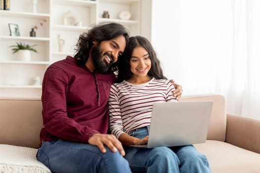 Loving cheerful indian couple using laptop together
