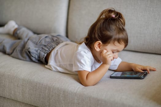 Adorable Toddler Baby Using Smartphone While Relaxing On Couch At Home