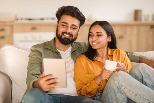 Hindu couple with tablet and coffee on sofa