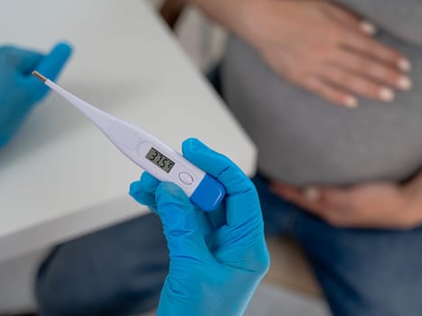 Pregnant woman with fever at doctor's appointment. Therapist holds an electronic thermometer with a temperature of 37.5.