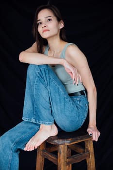 a woman in denim pants sits on a chair on a black background