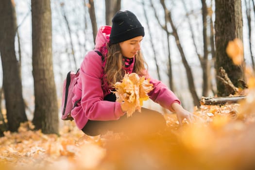 Young woman in a hat collects autumn leaves. Fall season concept. Generation Z and gen z youth