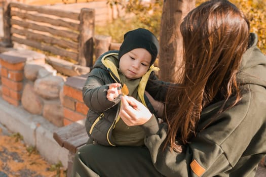 Cute little asian boy with mother outdoors. Happy child walking in autumn park. Toddler baby boy wears trendy jacket and hat. Autumn fashion. Stylish child outside.