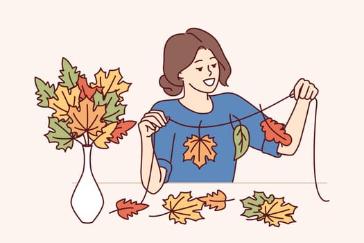 Woman creates autumn atmosphere in home by making handmade garland from colorful tree foliage