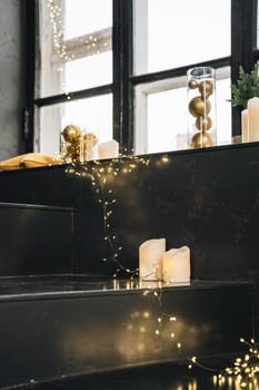 Black windowsill decorated for Christmas with golden baubles and candles