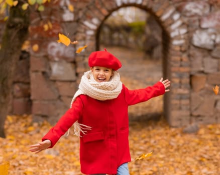 Happy caucasian girl in a red coat and beret walks in the park in autumn.