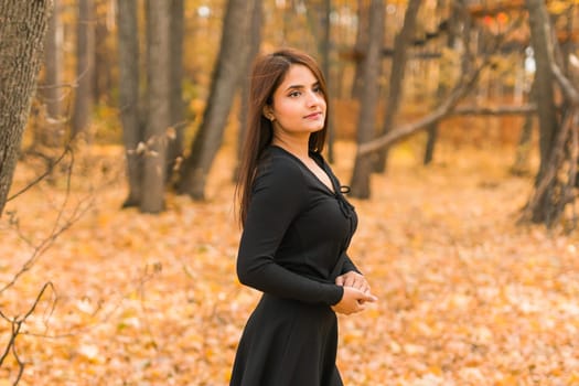 Beautiful indian woman generation z relaxing and feeling nature at autumn park in fall season. Diversity and gen z youth