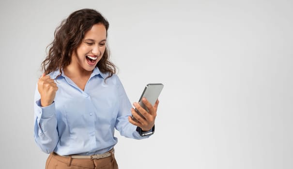 Happy young european woman with open mouth look at phone, celebrate success, win with fist raised up