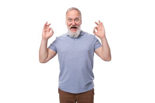 grandfather with a gray beard and mustache in a t-shirt and trousers joyfully and with astonishment shows a gesture of ok