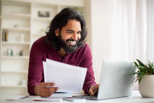 Smiling Young Indian Man Working With Papers And Laptop At Home Office