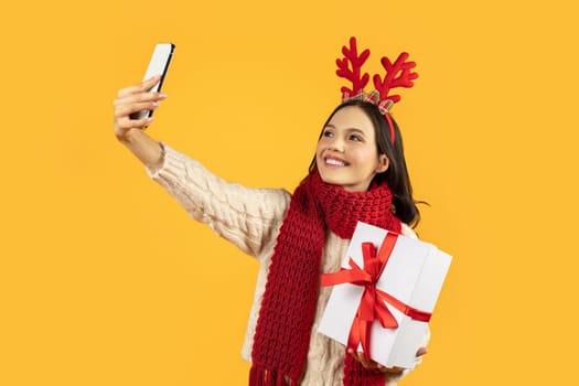 woman in festive deer antlers takes selfie on yellow background