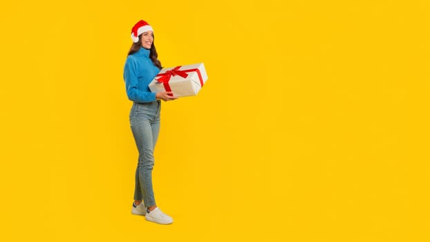 Woman stands with wrapped Xmas gift on yellow studio background